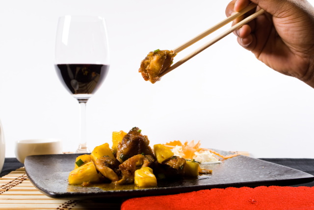 Dish of Chinese chicken with glass of red wine in background